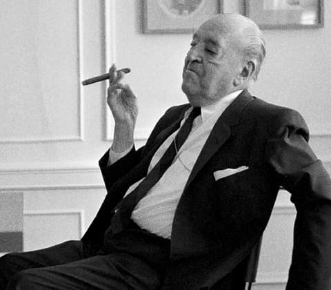 A portrait of Mies Van Der Rohe with a cigar in hand