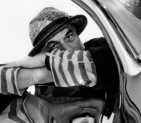 A portrait of Ron Arad peering through an abstract sinuous chrome sculpture